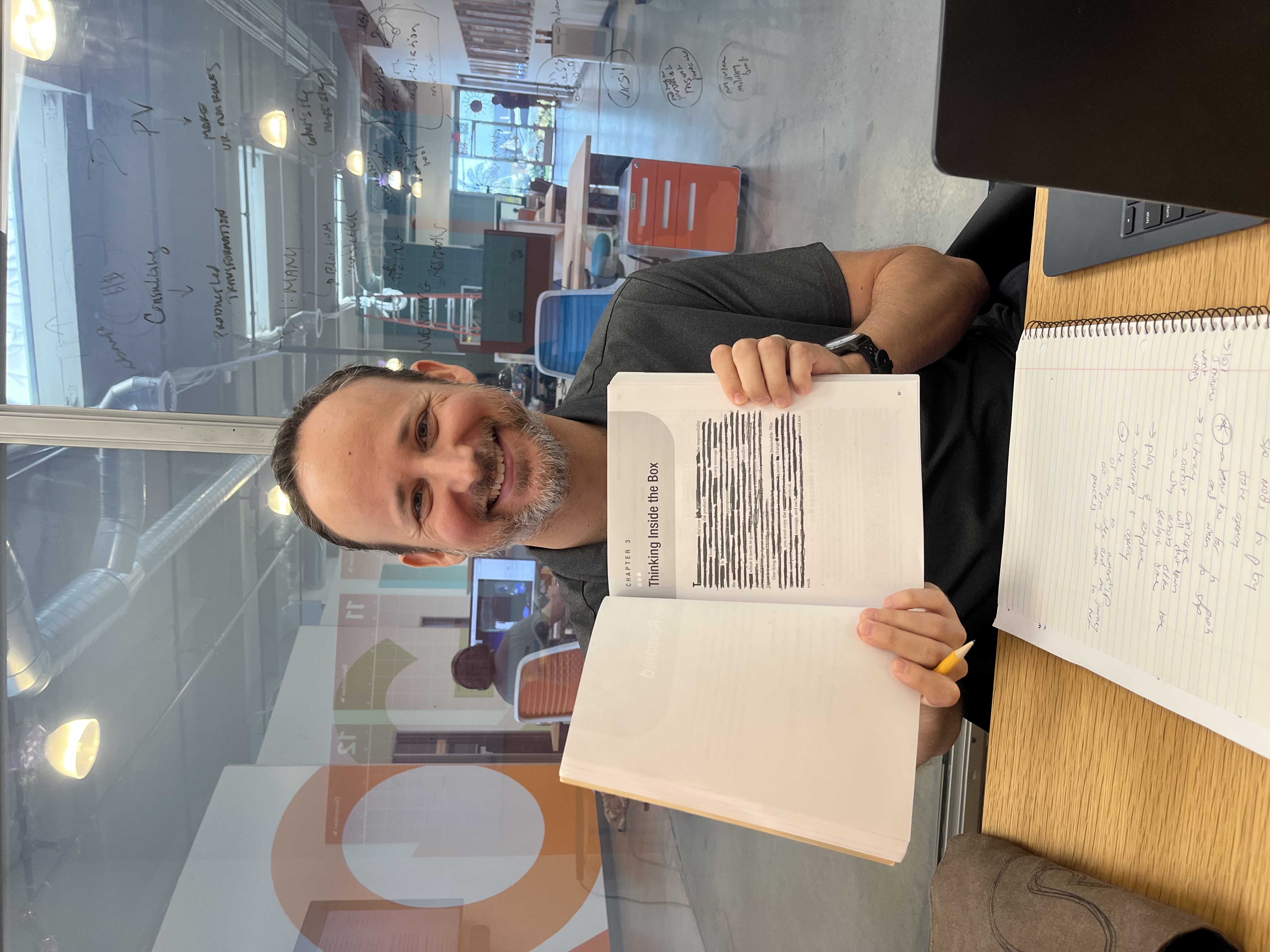 Jon smiling, holding open a technical book with his erasure poem blacked out on the page