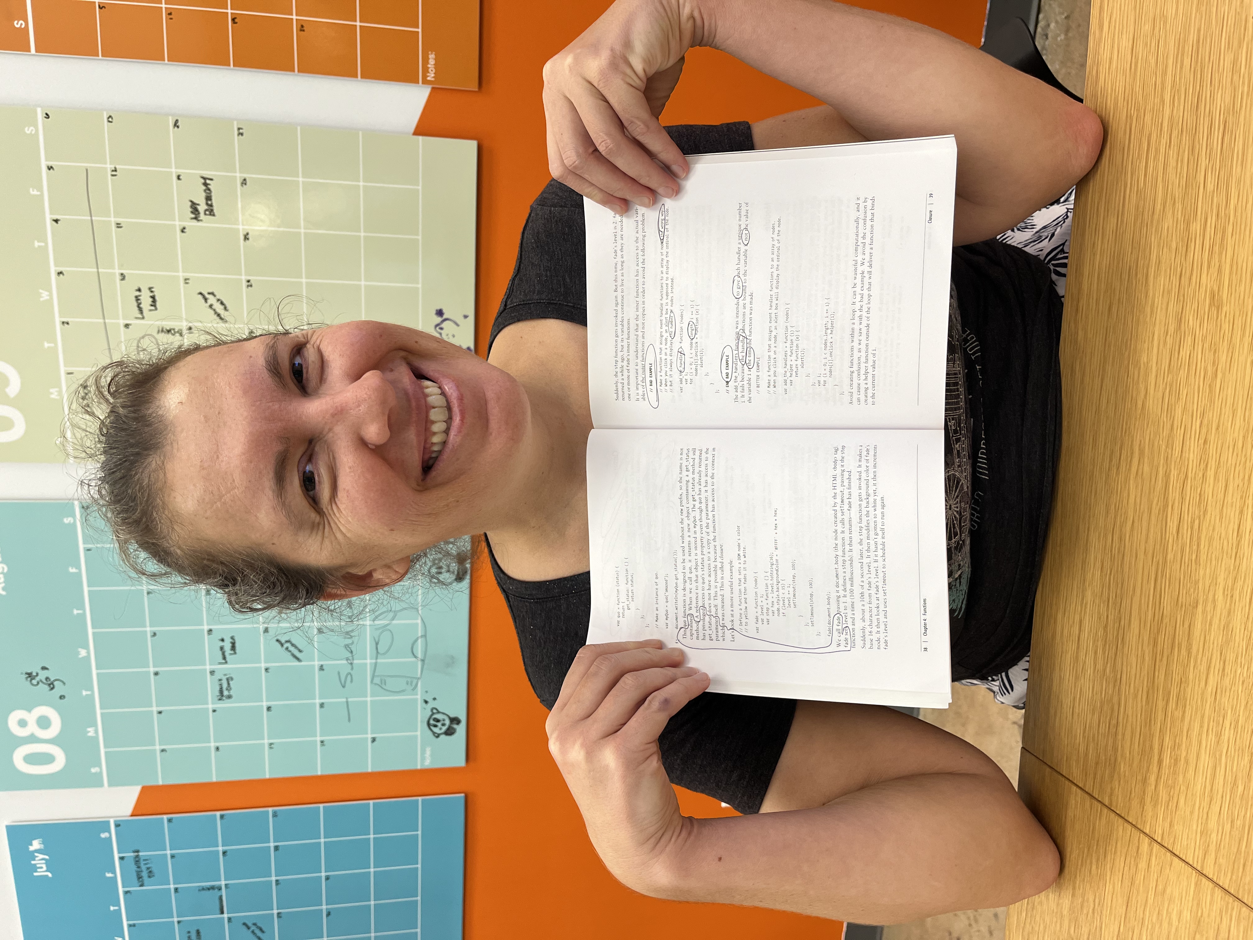 Sarah smiling, holding open a technical book with her erasure poem circled in pen across two pages